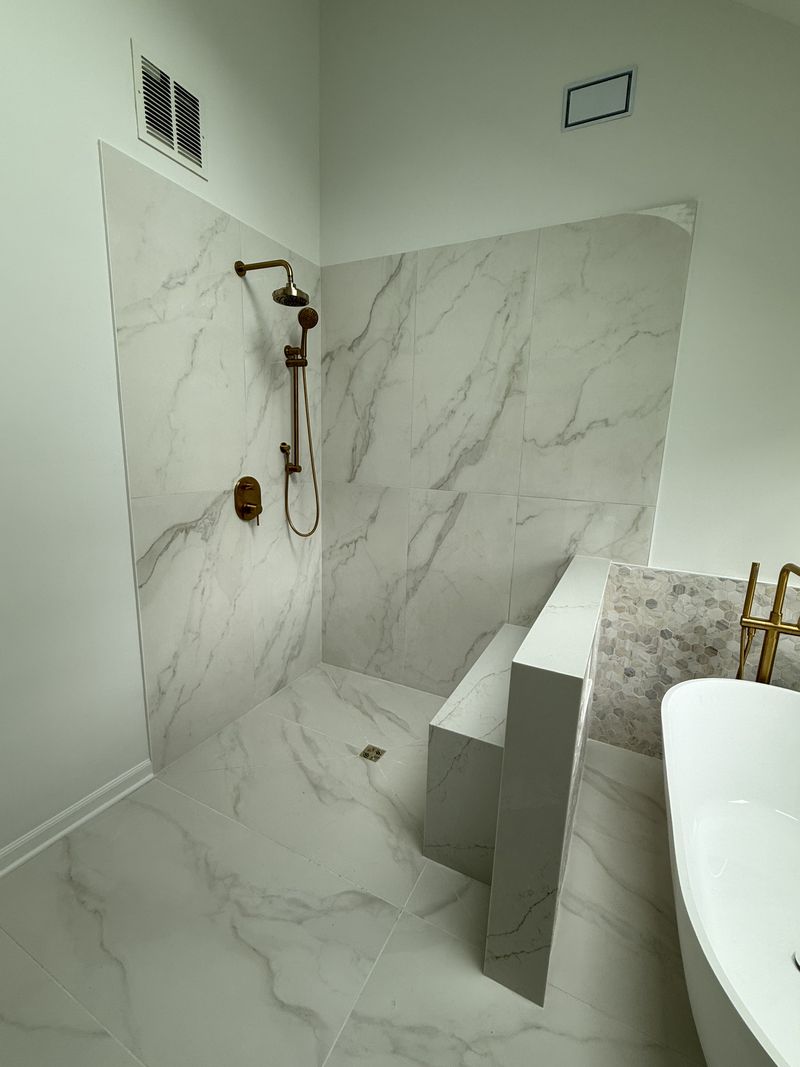 Curbless marble-look shower with brass fixtures and freestanding tub, bathroom remodel in southeastern Pennsylvania
