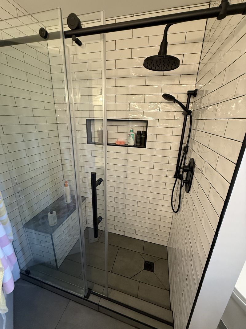 Subway tile shower with built-in bench and black sliding glass door, bathroom renovation in southeastern PA